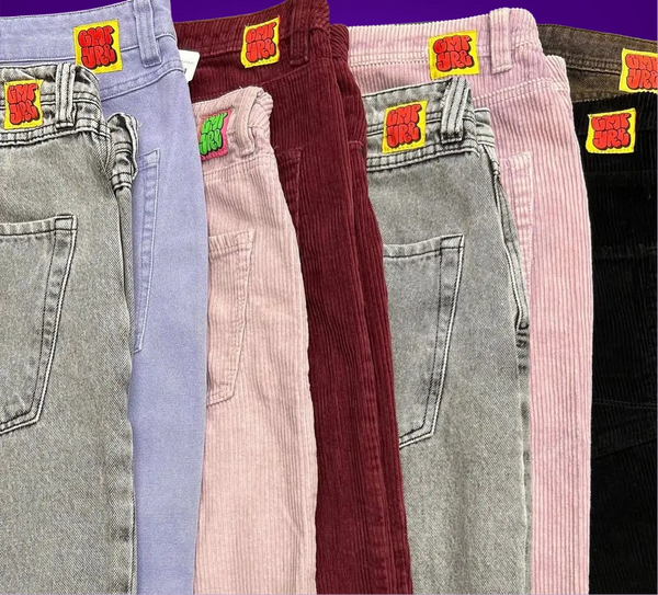 Five pairs of corduroy pants in different colors with colorful patches on a purple background.